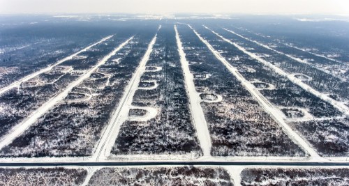 Aerial view of a snowy landscape with parallel lines and circular clearings in a forested area.