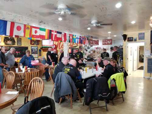 A busy diner with patrons seated at wooden tables, flags hanging from the ceiling, and a warm, inviting atmosphere.