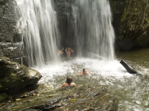 People swimming near a waterfall, surrounded by rocks and flowing water in a natural setting.