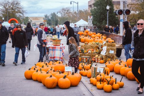 A bustling outdoor market with people, pumpkins, and festive decorations during a fall event.