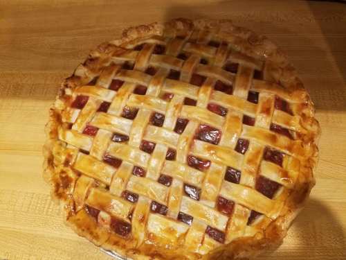 A freshly baked pie with a golden lattice crust and berry filling, resting on a wooden surface.