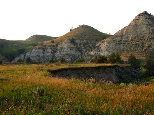 A serene landscape featuring rolling hills, grassy fields, and rocky formations under a soft sunset glow.