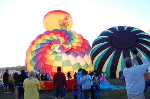 Colorful hot air balloons being inflated at a festival, with spectators watching in the foreground.