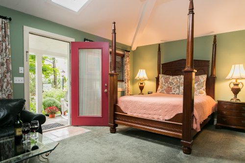 Cozy bedroom with a four-poster bed, green walls, and a red door leading to a garden view.