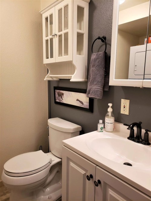 A small bathroom featuring a toilet, sink with cabinet, wall art, and a towel rack against a gray wall.