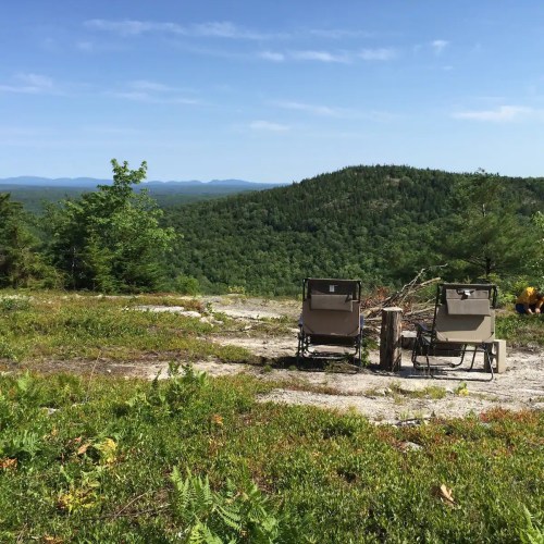 Two empty chairs facing a scenic view of green mountains and a clear blue sky.