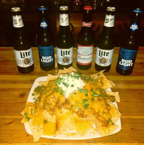 A plate of nachos topped with cheese, sour cream, and green onions, surrounded by various beer bottles.
