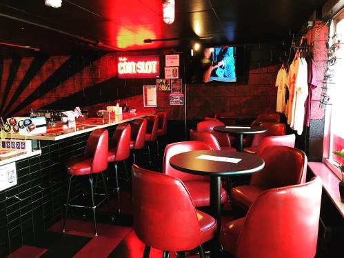A cozy bar interior with red chairs, a black counter, and a TV, featuring a vibrant atmosphere and stylish decor.