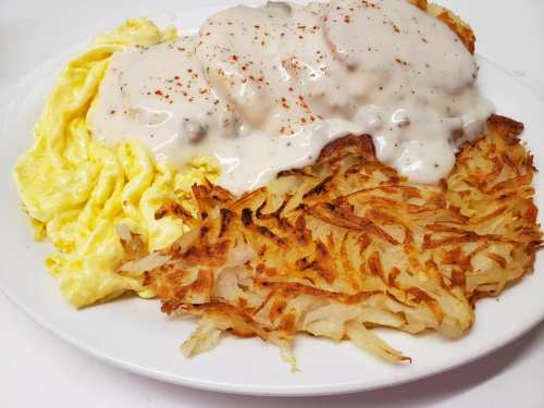 A plate of fluffy scrambled eggs, crispy hash browns, and creamy sausage gravy.