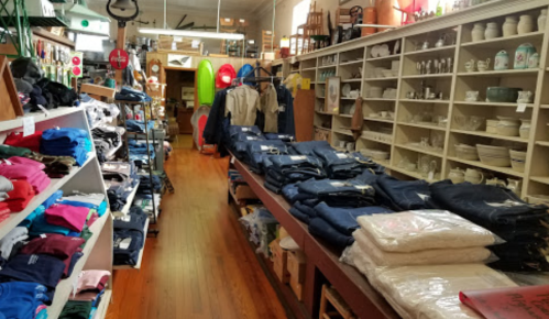 A cozy store interior filled with clothing, home goods, and outdoor gear, featuring wooden floors and shelves.
