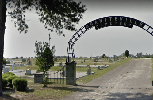 Entrance to Graniteville Cemetery, featuring a stone archway and a pathway lined with gravestones and greenery.