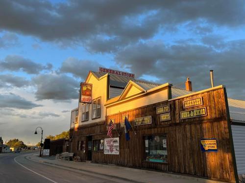 A rustic general store with wooden siding, flags, and a sign, set against a cloudy sky at sunset.