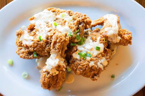 Crispy fried chicken pieces drizzled with creamy sauce and garnished with chopped green onions on a white plate.