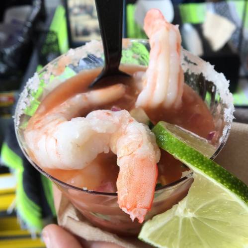A close-up of a shrimp cocktail in a clear cup, garnished with lime and served with a spoon.