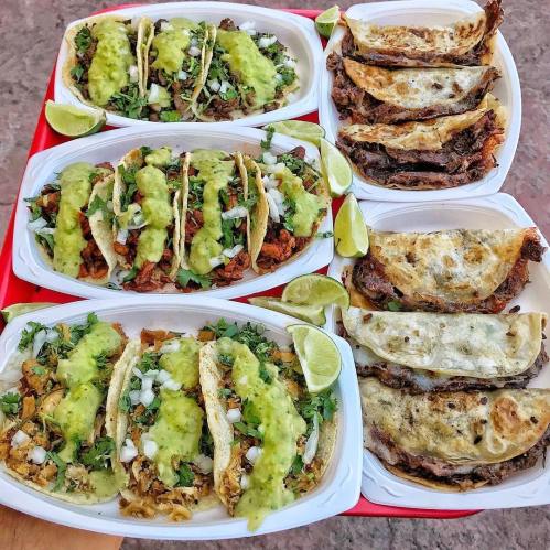 A tray of tacos featuring various fillings, topped with green sauce and garnished with lime wedges.