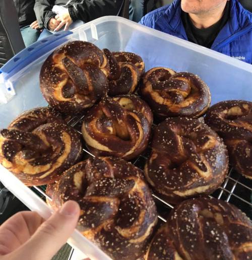 A hand holds a container of freshly baked pretzels, with a person in the background.
