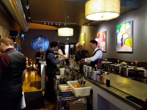 A lively bar scene with bartenders mixing drinks, colorful artwork on the walls, and a cozy atmosphere.