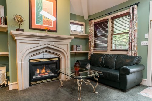 Cozy living room with a fireplace, black leather sofa, glass coffee table, and green walls adorned with artwork.