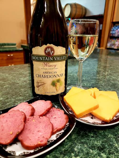 A bottle of Mountain Valley Winery Chardonnay with a glass, alongside sliced meats and cheese on a plate.