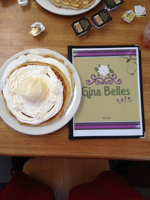 A plate of pancakes topped with whipped cream and ice cream, next to a menu for Gina Belles Cafe.