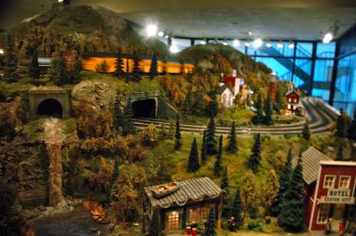 A detailed miniature landscape featuring hills, tunnels, a train, and small buildings among trees and a waterfall.