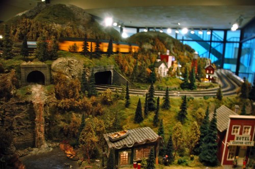 A detailed miniature landscape featuring hills, tunnels, a train, and small buildings among trees and a waterfall.