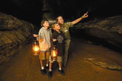 Two children hold lanterns while a guide points out features in a dark cave.