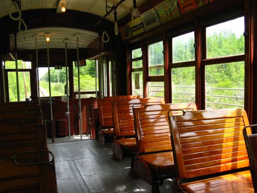 Interior of a vintage train car with wooden benches and large windows, showcasing green scenery outside.