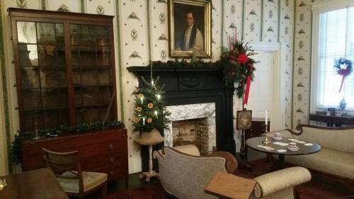 Cozy room with a fireplace, decorated Christmas tree, vintage furniture, and festive holiday decor on the walls.