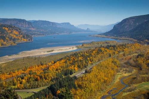 A scenic view of a river winding through vibrant autumn foliage and mountains under a clear blue sky.