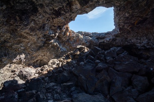 A rocky cave with a large opening at the top, revealing a clear blue sky above.