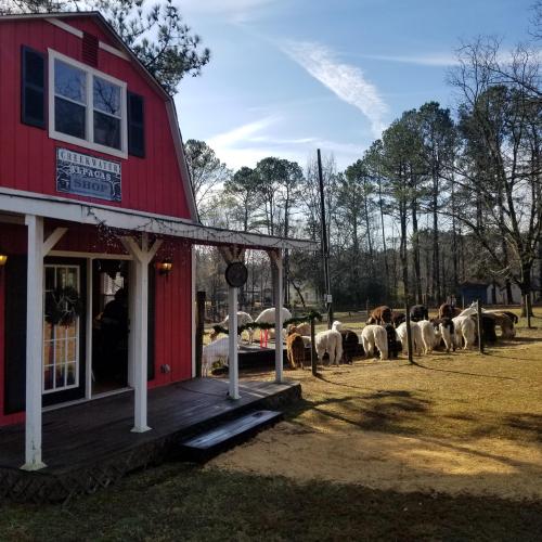 A red shop with a porch, surrounded by trees and a group of animals grazing nearby under a blue sky.