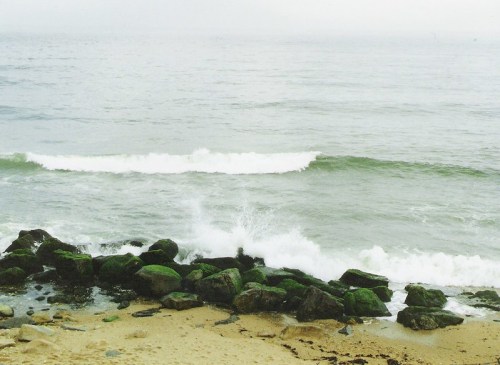Waves crash against rocky shore under a foggy sky, creating a serene coastal scene.