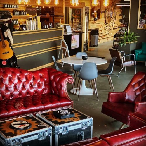 Cozy café interior with red leather sofas, wooden decor, and a mix of tables and chairs under warm lighting.