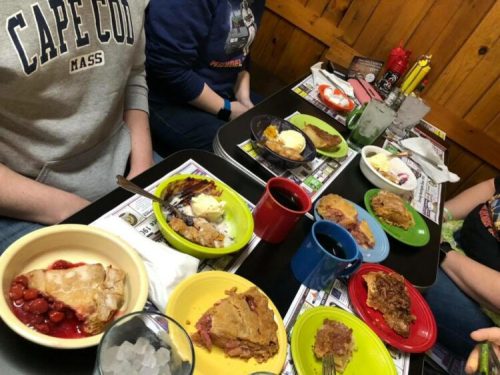 A table filled with colorful plates of food, desserts, and drinks, with people seated around it.