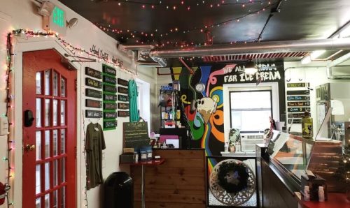 A cozy shop interior with colorful lights, a mural, and a counter displaying merchandise and a menu board.