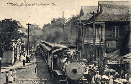 A vintage postcard showing a train arriving in Covington, Louisiana, with people gathered on the street.