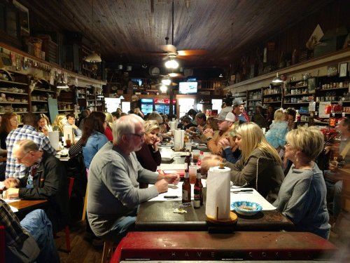 A busy restaurant interior with diners at tables, surrounded by shelves filled with various items and decor.