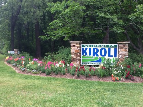 Welcome sign for Kiroli Park surrounded by colorful flowers and greenery.