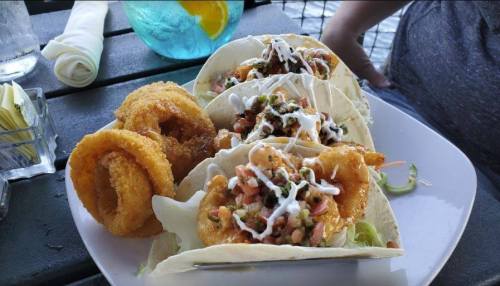 Three shrimp tacos topped with pico de gallo and sauce, served with two onion rings on a white plate.