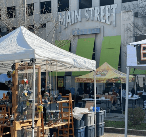 A market scene with a tent displaying crafts in front of a building labeled "Main Street." People are visible in the background.