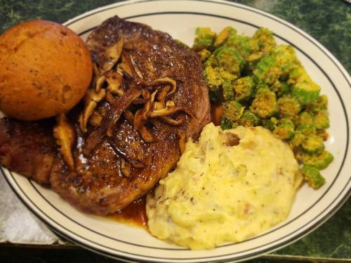 A plate featuring a steak with mushrooms, mashed potatoes, sautéed okra, and a cornbread muffin.