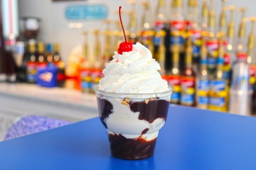 A delicious ice cream sundae topped with whipped cream and a cherry, served in a clear cup against a colorful background.