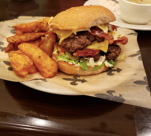 A juicy burger with cheese, bacon, and lettuce, served with crispy potato wedges on a plate.