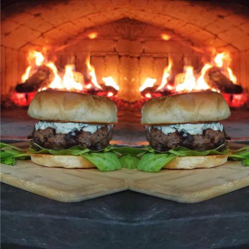 A delicious burger with lettuce and sauce, set against a backdrop of a glowing wood-fired oven.
