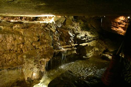 A dimly lit cave interior with flowing water and rocky formations, creating a serene underground landscape.