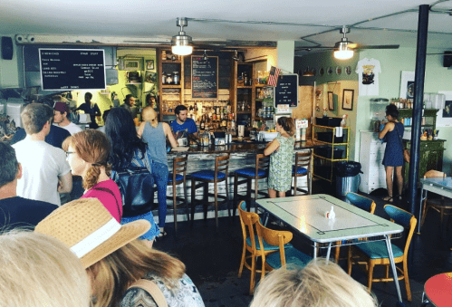 A busy café interior with patrons at the bar and tables, featuring a vibrant atmosphere and colorful decor.