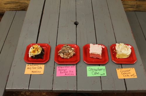 Four slices of cake on red plates: Holy Cow Cake, Peanut Butter Pie, Strawberry Cake, and Coconut Cream Cake, with prices.