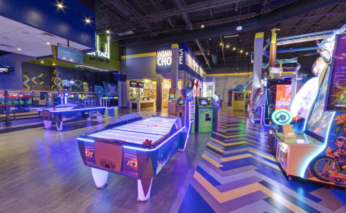 Brightly lit arcade with various games, including air hockey and colorful machines, in a fun, modern setting.