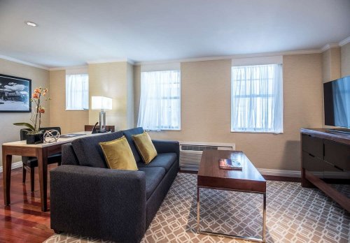 Cozy living area with a sofa, coffee table, and dining space, featuring large windows and warm lighting.